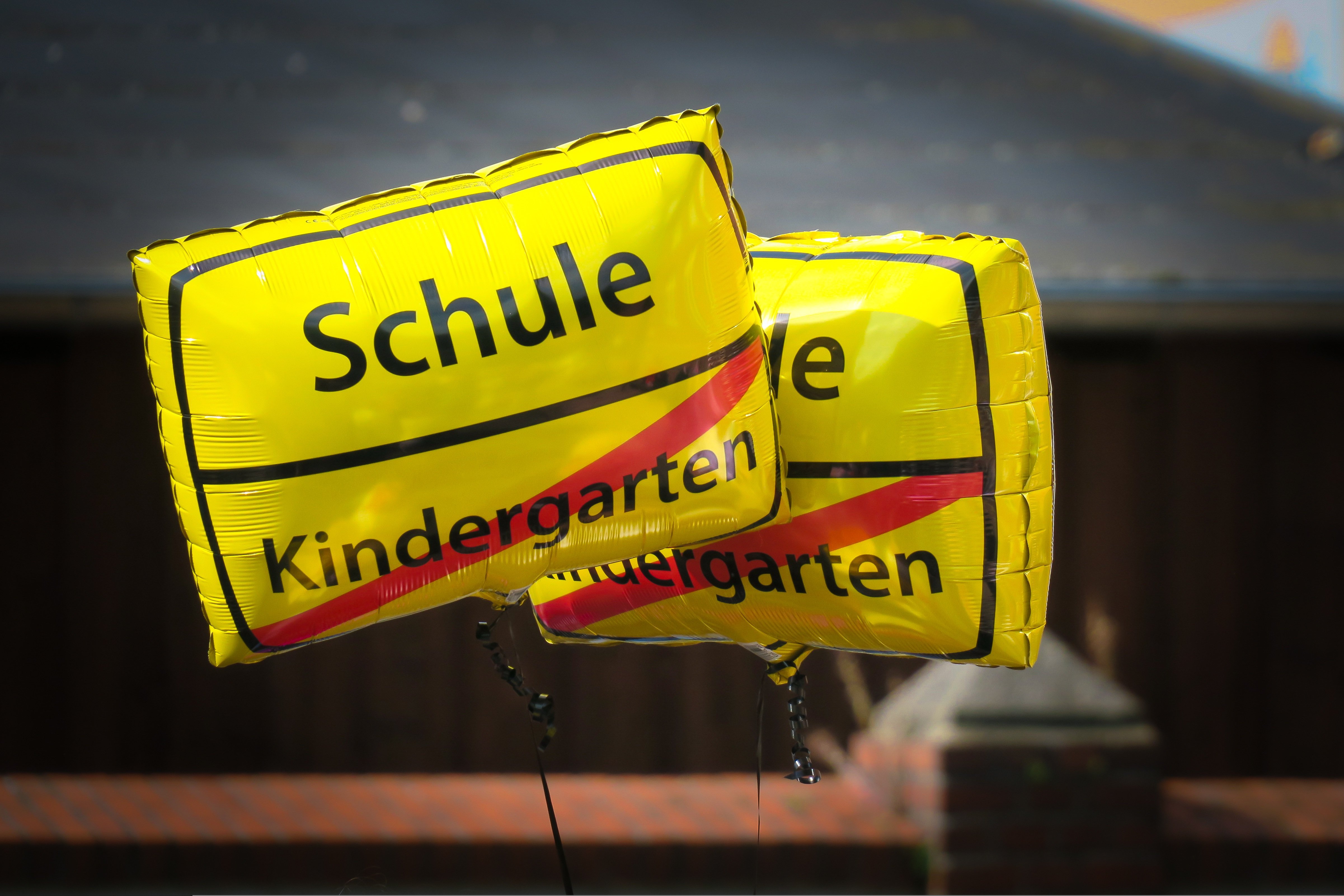 Luftballons mit Aufschrift in Ortsschildart: Schule, und Kindergarten, durchgestrichen
