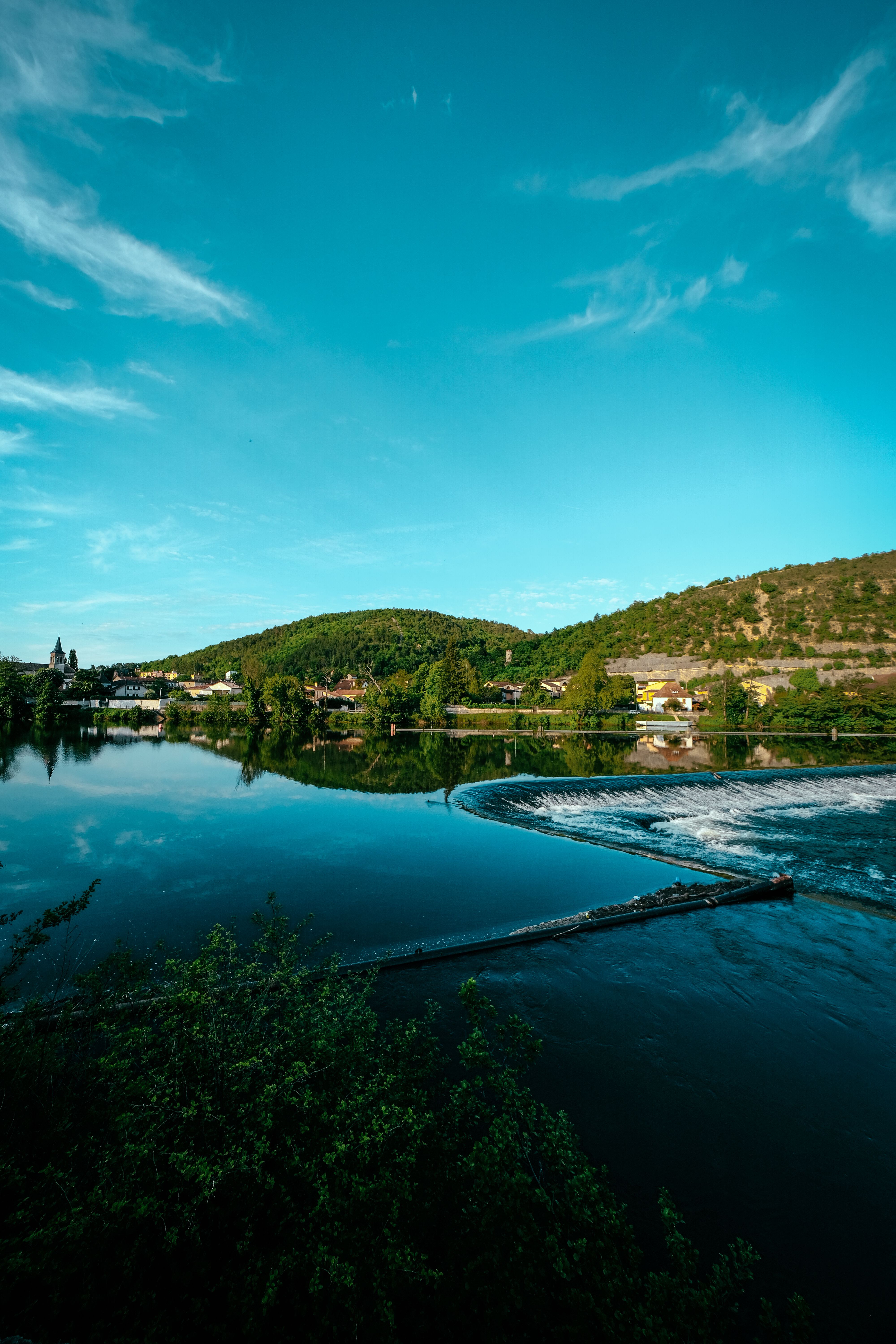 Serene Landschaft eines Dorfes am See mit üppigem Grün und blauem Himmel.
