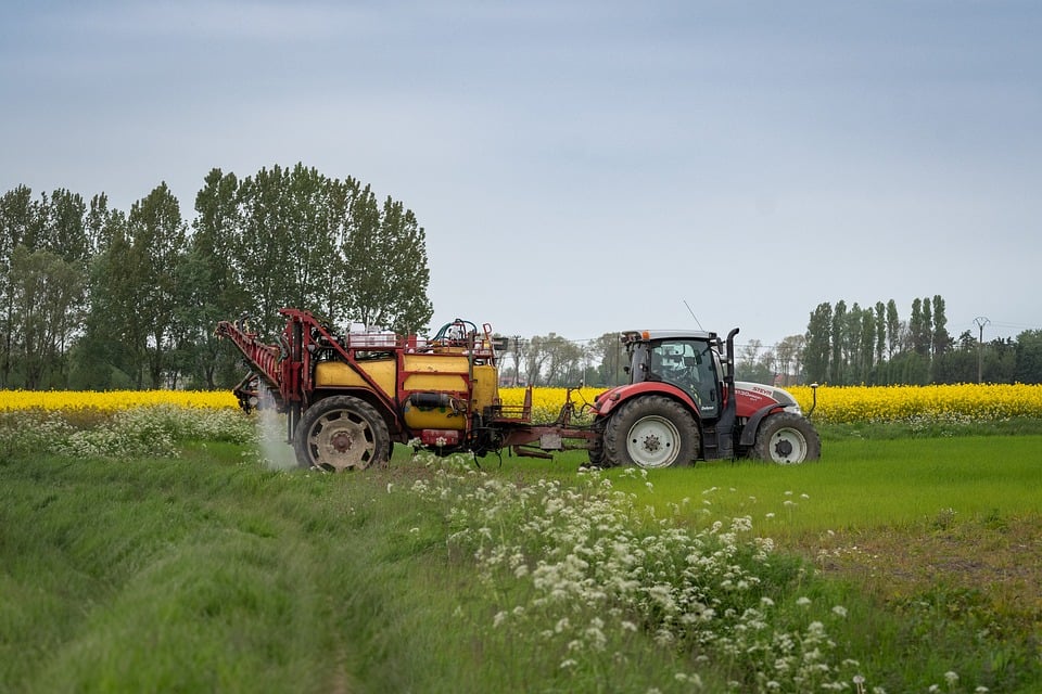 Ein roter Traktor fährt mit einer gezogenen Pflanzenspritze über ein Feld.